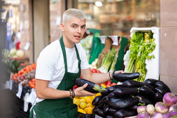 Grocery store employee places ripe eggplants on a display case at a street store