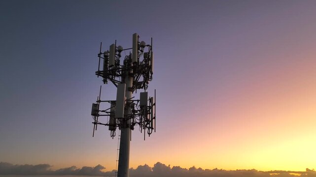 Cell tower at sunset along coast line. Drone shot rising from low to high tracking antenna array at top of cellular communications tower in Puerto Rico at dusk.