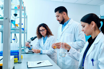 Multiethnic group of young adult scientists working together in laboratory, Caucasian woman using pipette, Hispanic man and Asian woman analyzing samples, scientific research in progress