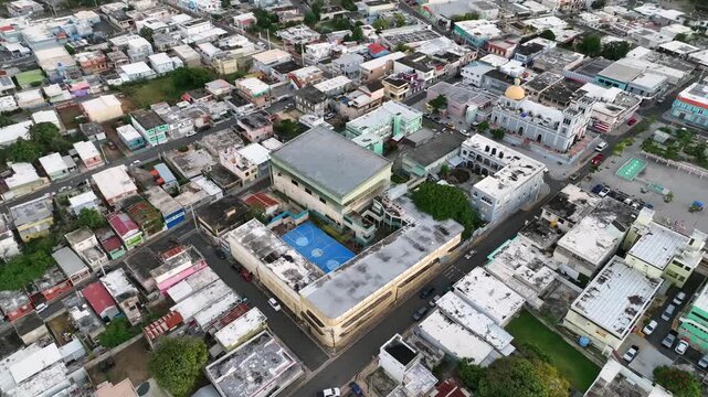 Aerial view of city streets and buildings in mid-sized town in Puerto Rico. Drone video flying backwards with high angle view of urban housing, schools and more in Isabella.