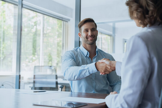 Fototapeta Young Latin bank worker man shaking hand with client, recruit employee on interview or business partner after signing contract. Group of people satisfied with results of team work together. Copy space