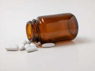 Spilled brown glass medicine bottle with white tablets on white background