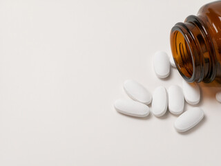 White tablets spilling from brown glass bottle on light background