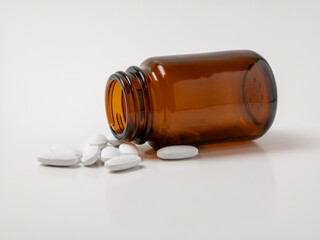 Brown glass medicine bottle with white pills spilled on white background