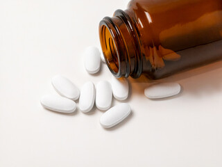 White tablets spilling from amber glass bottle on white background