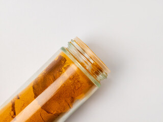 Glass jar of turmeric powder on white background