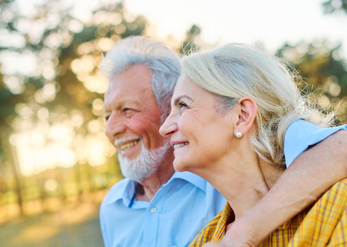 Happy active senior couple having fun talking and hugging sitting on a bench in park outdoors