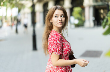 Fototapeta premium Happy woman in dress looking around city street on summer day