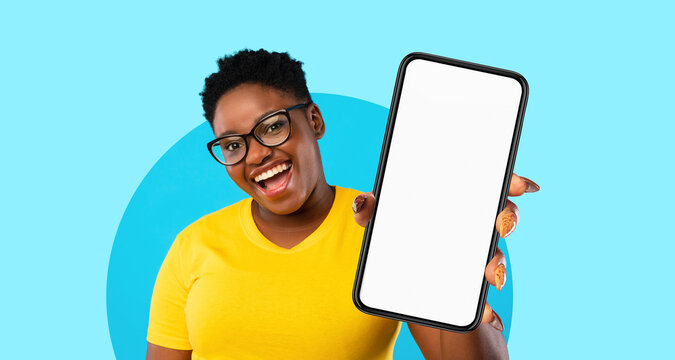 A woman with short curly hair wears glasses and a bright yellow shirt. She smiles widely while holding a blank mobile device in front of her against a vibrant blue backdrop.