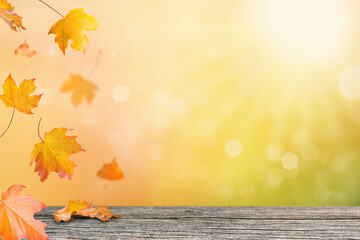 Autumn background with colorful falling maple leaves and wooden table. Bright sunlight and bokeh create a warm seasonal atmosphere
