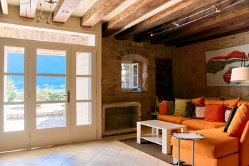 Cozy Living Room with Bright Orange Sofa Overlooking Scenic View Through Open Doors in a Stone-Finished Home