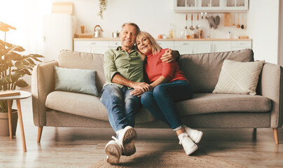Happy Mature Couple Embracing Posing Sitting On Couch At Home, Smiling Looking At Camera....