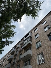 Soviet era residential apartment building with balconies and trees, typical urban housing architecture under cloudy sky
