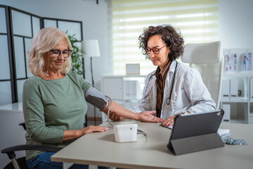Obraz premium Female doctor checking blood pressure of senior woman in the doctors office