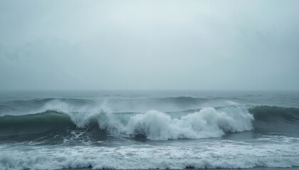 Fototapeta premium Misty ocean waves crash on shore. Powerful water surge under a cloudy sky. Serene marine scene feels tranquil and dramatic, grey tones dominate.