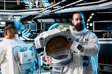 Portrait of astronaut holding helmet preparing for scientific mission, operating spacecraft. Spaceship crew member in spacesuit wearing equipment preparing for planetary exploration mission © DC Studio