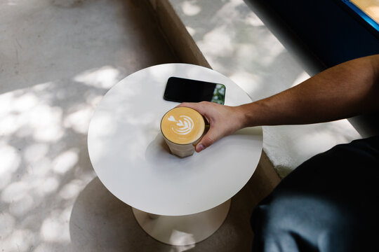 Anonymous person holding a latte art coffee inside a modern caf&eacute;