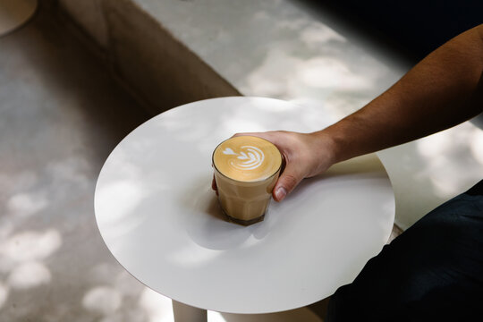 Anonymous person's hand holding a latte decorated with latte art