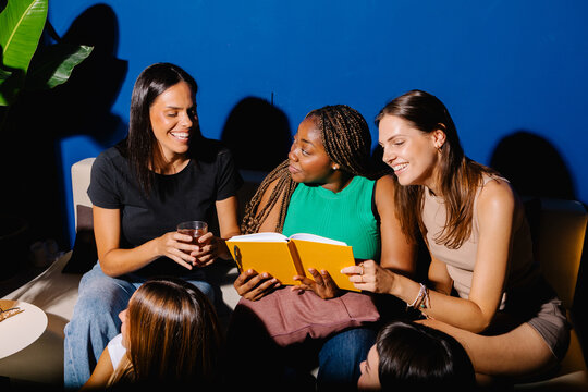 Female team relaxing in a communal office area, browsing a book