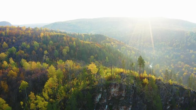aerial view of the South Ural Mountains in the Republic of Bashkortostan, Russia, showcasing a vibrant autumn forest with golden, orange, and green foliage under the warm glow of sunlight.