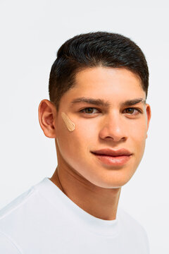 Young Latino man with visible foundation swatch on cheek
