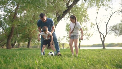 family playing football. people parks and nature concept. young father with his daughter and son playing with a soccer ball in nature, running on the grass and lifestyle laughing