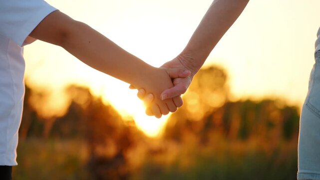 Carefree little kid holding mother hand when walking in summer day outside.