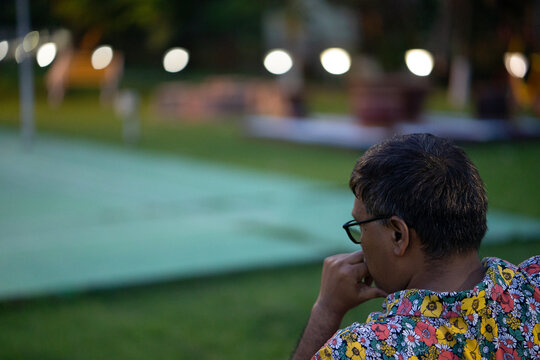 Indian middle aged man sit on a bench in park and deeply thinking 