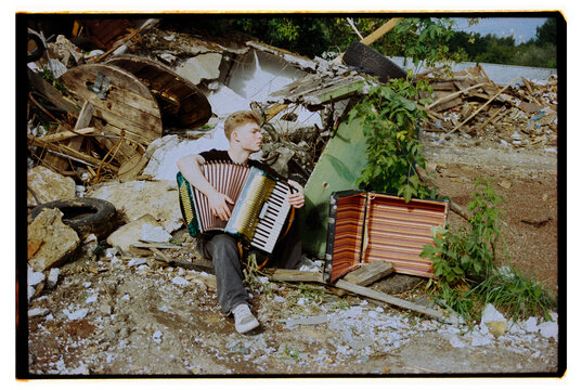 Young musician plays accordion in rubble