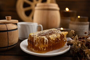lose-up of a honeycomb on a white plate surrounded by a wooden barrel and a cup. a warm and rustic atmosphere. Bee honey.