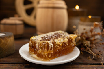 lose-up of a honeycomb on a white plate surrounded by a wooden barrel and a cup. a warm and rustic atmosphere. Bee honey.