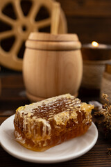 lose-up of a honeycomb on a white plate surrounded by a wooden barrel and a cup. a warm and rustic atmosphere. Bee honey.