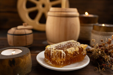 lose-up of a honeycomb on a white plate surrounded by a wooden barrel and a cup. a warm and rustic atmosphere. Bee honey.
