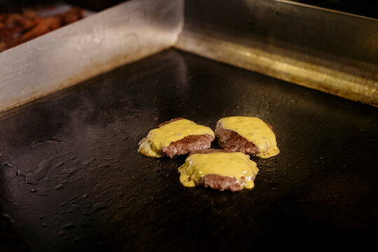 Cooking beef patties on a griddle inside a kitchen
