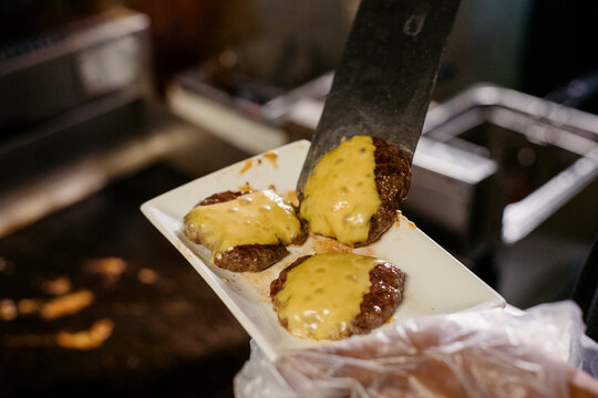 Chef prepares beef patties with melted cheese inside a kitchen