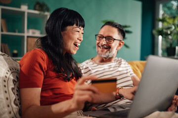 Happy couple shopping online using laptop and credit card at home