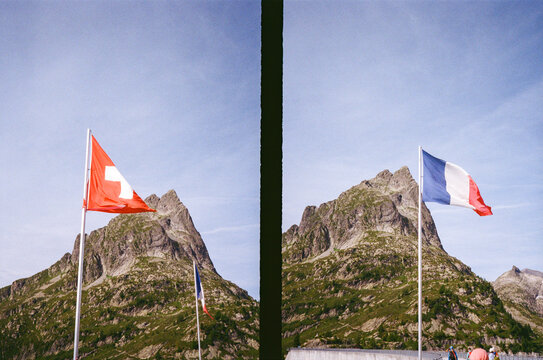 Swiss and French Flags Waving Against a Mountain Backdrop