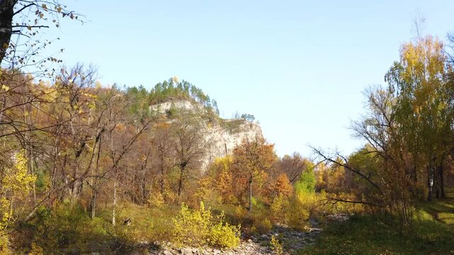 Footage capturing the vibrant autumn colors of the Kyzyltash Mountain Range in the South Ural region of Russia. The scene features a picturesque natural landscape with trees adorned in yellow and oran