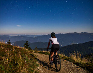 Young cyclist riding on a mountain trail at starry night