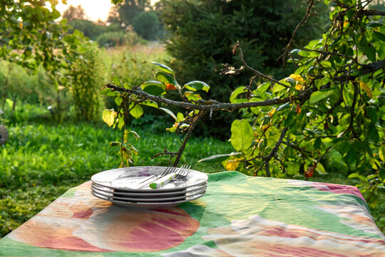 Meal Outside. Table with Stack of Plates Against a Green Garden