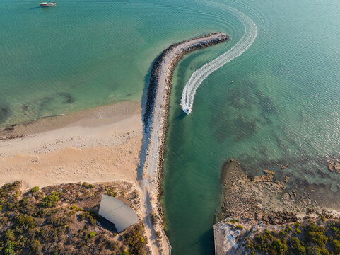 Boat speeding alongside a rock breakwater and beach