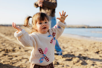 Toddler girl raising hands with dirty palms playing on beach in fall