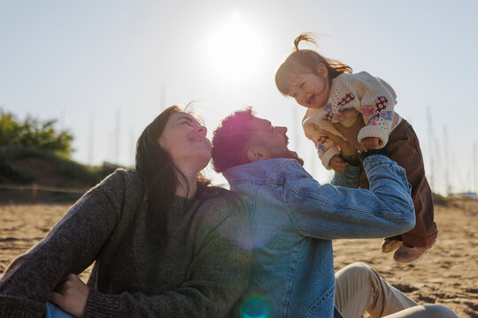 Happy family lifting baby daughter on beach at sunset