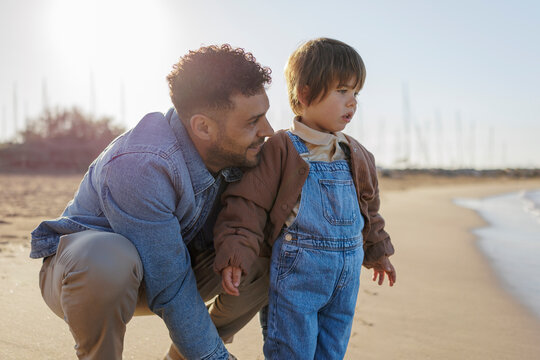 Father and son admiring seascape on sunny beach during fall season