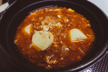 A delicious Korean gourmet plate featuring a hot red tofu soup dish, a tasty meal with chili sauce