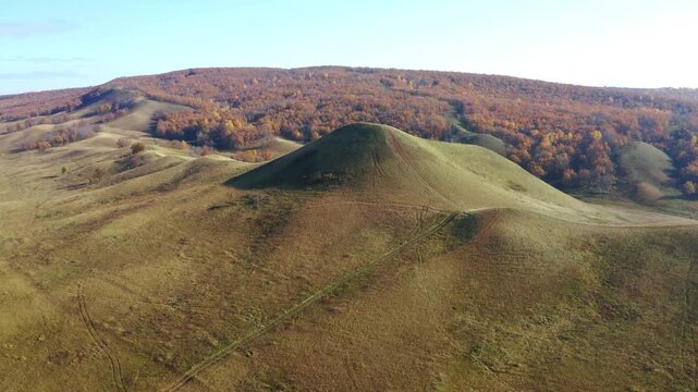 An aerial drone shot captures the unique conical shape of Juraktau, one of the four Shihan hills in the South Ural region of Russia. The footage shows the hill covered in green and yellow grass, with 