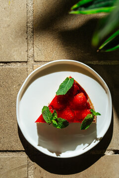 Slice of strawberry tart with mint on white plate 