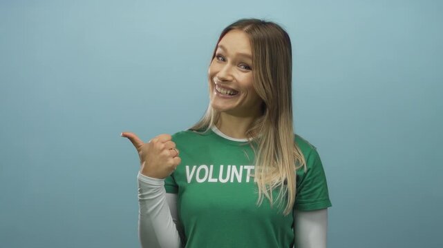 Smiling woman wearing green volunteer shirt giving thumbs up on blue isolated background