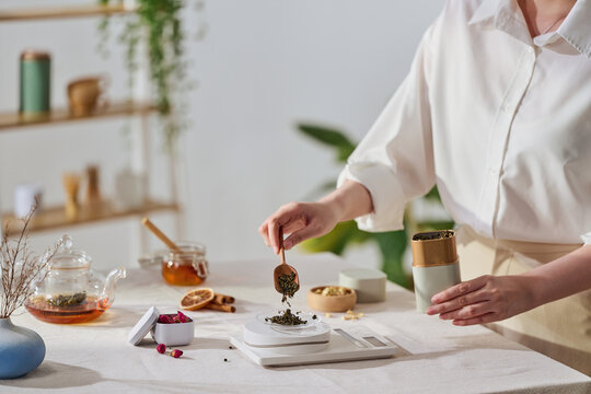A person measuring tea leaves with a wooden spoon and a digital scale