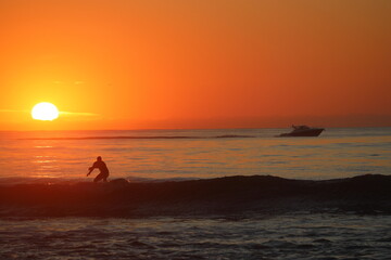 Fototapeta premium silhouette of a surfer and boat with sunrise background